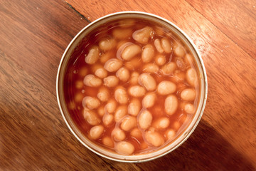 Open can of baked beans on wooden background
