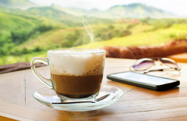 Cup of cappuccino on table over mountains landscape with sunligh