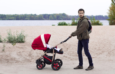 The father walks with the baby in the baby carriage in the park