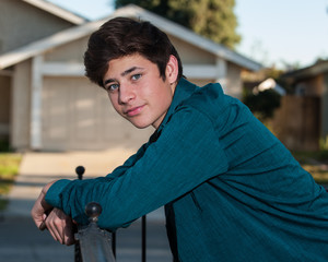 Handsome Latino teen leaning on handrail looking to left.