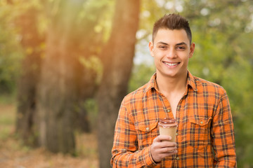 Cheerful young man with coffee in park in autumn