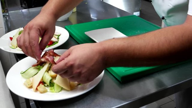Chef put the slices of bacon on the chopped vegetables, parmesan, cheese, chicken, cherry tomatoes, lettuce, cook prepares on the professionally kitchen Restaurant, chef prepares
