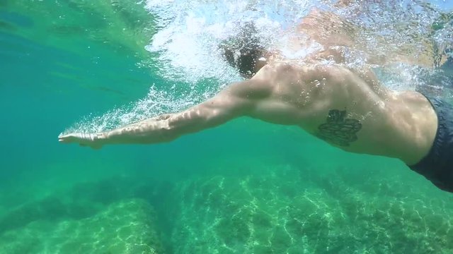 UNDERWATER: Sporty guy swimming crawl with eyes shut in beautiful emerald ocean