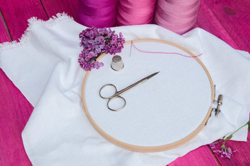 Pink thread and white fabric in the wooden embroidery frame for