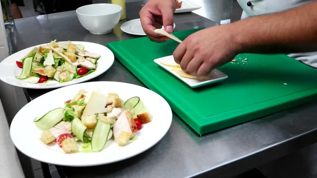 Caesar salad, chef put the cheese, parmesan on sauce and chopped vegetables, chicken, cherry tomatoes, lettuce, cook prepares on The professionally kitchen restaurant, chef prepares