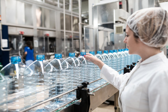 Water bottling line for processing and bottling pure mineral water into bottles. Female worker checking out water bottles. 