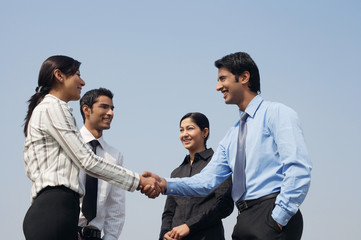 four business colleagues, two shaking hands