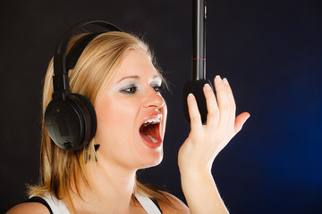 Woman singing to microphone wearing headphones in studio