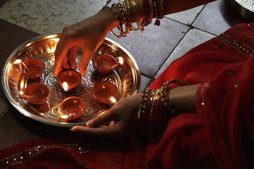 Close up of woman wearing a sari, putting oil lamps on silver tray