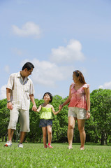 Family with one child walking in park, holding hands