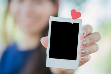 Woman hold  photo instant on hand. Blank instant photo and red clip paper heart. relationship concept.