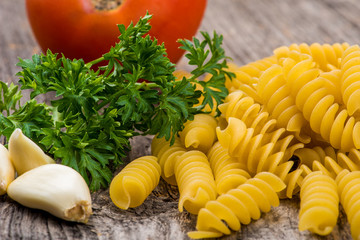 Pasta, garlic, tomato and parsley on wood background