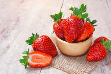 Fresh strawberries in a bowl decorated by cut strawberry on rustic wooden table.
