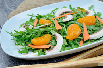 salad arugula with mushroom and mandarin in white dish on gray wooden table