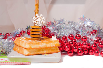 Christmas waffle with honey on ceramic plate . decorate by red garland ,tinsel with snow flake. Served with honey spoon and napkin