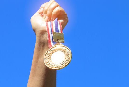 hand raised and holding gold medal against blue sky. award conce