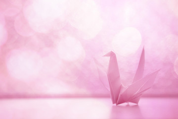 origami paper bird on the bright-lit glass window with pink solf