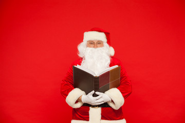 Santa Claus reads old book, on a red background. Christmas