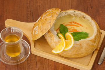 homemade cream soup garnished with lemon slices in a bread bowl on a board and a cup of green tea