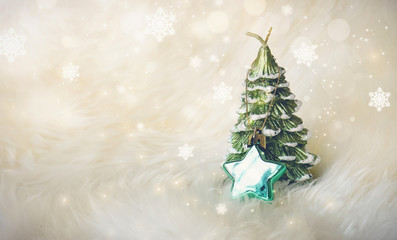 Small Christmas tree with a green star on white fur, surrounded with glitter star dust and snowflakes