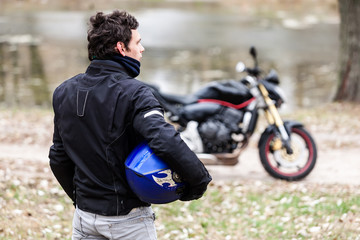Biker standing near motorcycle holding his blue helmet.