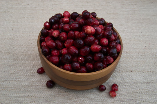 Fresh Red and Maroon Cranberries Heaped in Turned Wood Bowl Against Beige Woven Fabric Background From Above with Loose Berries, 