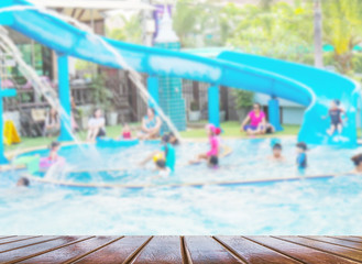 Blurred photo of people playing in a swimming pool fun park with brown wood terrace