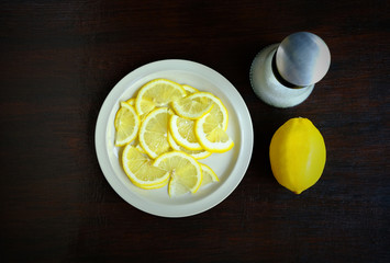 Overhead view of sliced lemon in a white dish with salt shaker on a wooden table, Food ingredient image