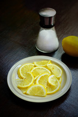 Sliced lemon in a white dish with salt shaker on a wooden table, Food ingredient image