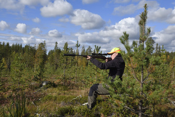 Young female moose hunter sitting on a stump aiming with her rifle with silencer ,picture from the...