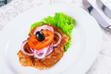 Fried beef with onion rings, tomato and lettuce leaves on white plate. Armenian food. Kofta