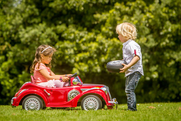 young happy children - boy and girl - driving a toy car outdoors