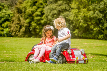Naklejka na ściany i meble young happy children - boy and girl - driving a toy car outdoors
