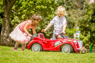 young happy children - boy and girl - driving a toy car outdoors