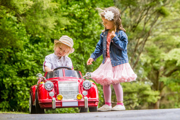 young happy children - boy and girl - driving a toy car outdoors