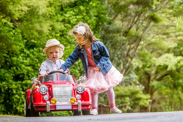 young happy children - boy and girl - driving a toy car outdoors