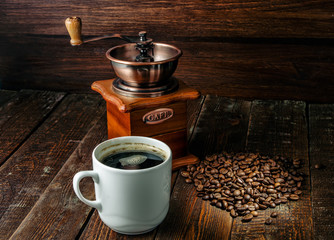 Coffee cup with coffee mill and caffee beans on dark wood background