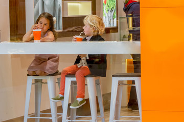two young happy kids, boy and girl, in a cafe, drinking juice