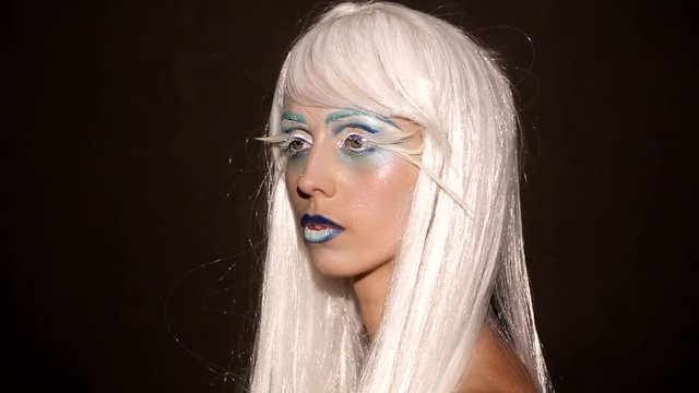 Beautiful woman with blue and white metallic makeup, long false lashes behind peacock feathers