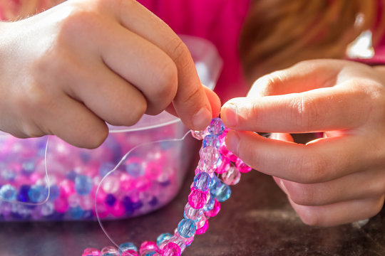 young child girl making bead bracelet, indoor portrait