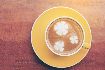 Top view of cup of coffee on wooden table with flower milk decoration on top of coffee surface