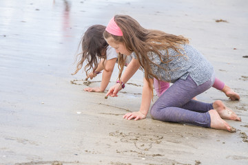 Fototapeta premium outdoor portrait of young girl drawing in sand on natural sea ba