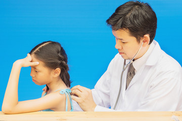 Sick Asian girl is being treated by male doctor over blue background