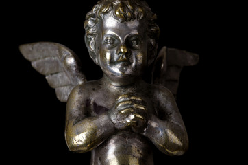 Fototapeta na wymiar Praying winged putto on black background. Angel made of brass, covered with silver, as part of a candelabra from nineteenth century and symbol for religious passion. Macro object photo front view.