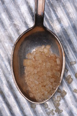 Silver spoonful with brown sugar on metal table closeup
