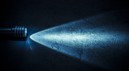 Flashlight and a beam of light in darkness. A modern led light with bright projection on dark stone...