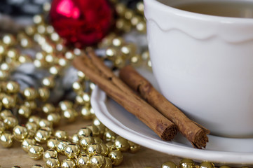 Two cinnamon sticks near white cup of green tea among christmas decoration