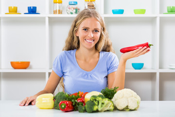 Beautiful girl is sitting at the table with bunch of vegetable.
