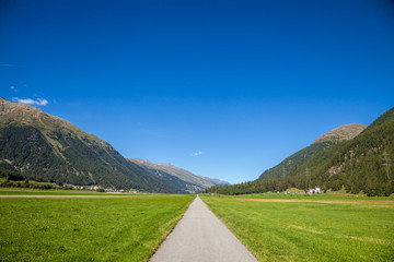 Straight road through valley in Switzerland with mountain range in background