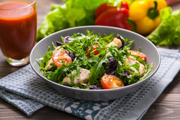 Fresh salad with chicken, tomatoes, arugula, mesclun, basil and tomato juice on a cloth napkin, on wooden table